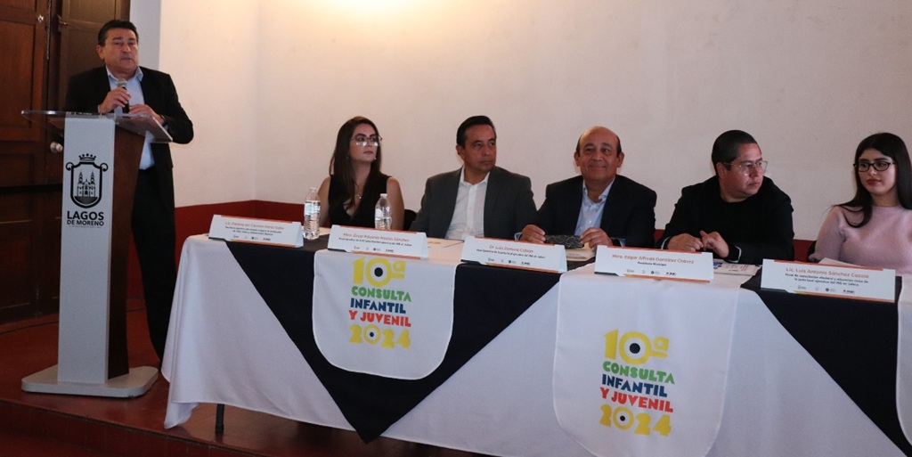 un hombre de pie, junto a cinco personas sentadas a su lado