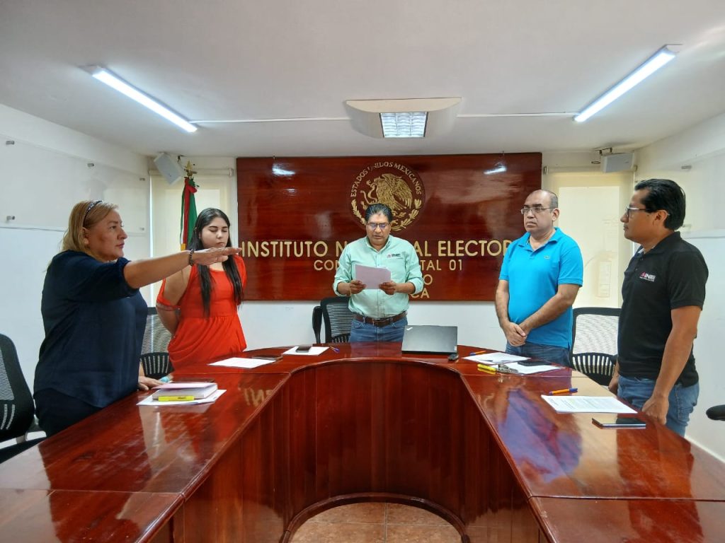 dos mujeres y tres hombres de pie, una mujer con el brazo derecho extendido al frente