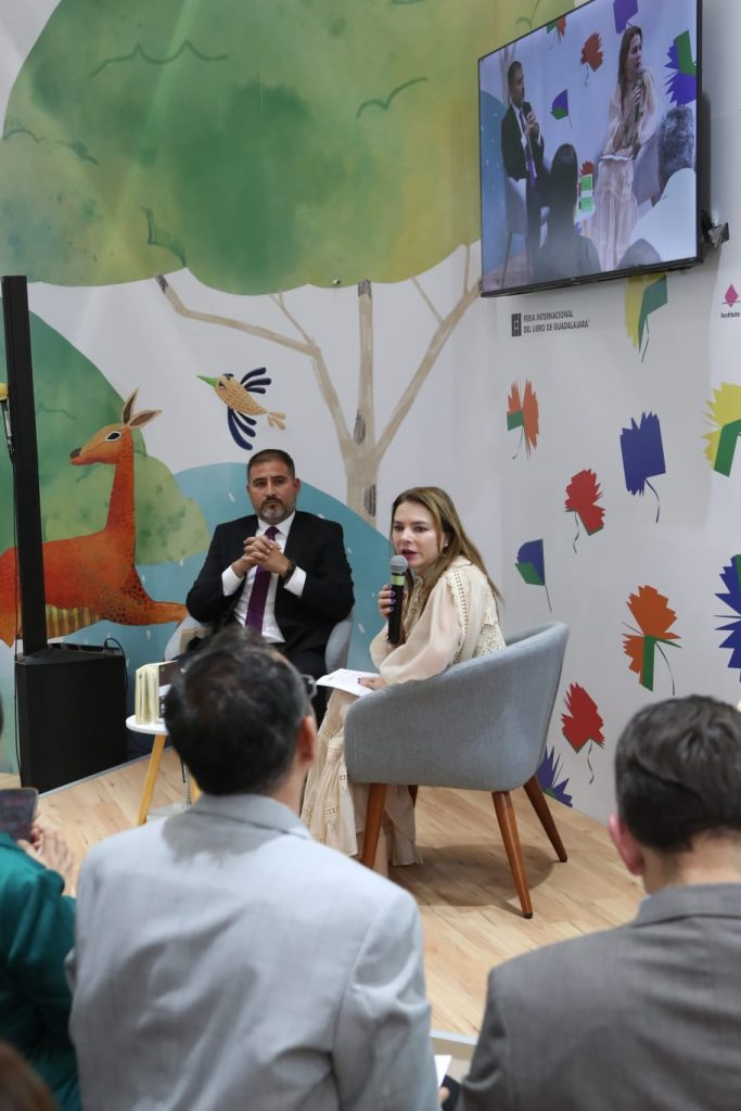 Personas participantes sentadas en el estrado enfrente del público asistente participando en el evento.