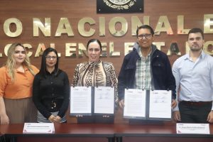 tres mujeres y dos hombres de pie, en medio una mujer y un hombre sostienen un documento