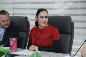 mujer cabello negro recogido sentada frente a una mesa con micrófono