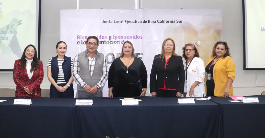 seis mujeres y un hombre de pie frente a una mesa con mantel negro y documentos