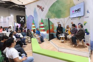 Personas participantes sentados en el estrado frente al público asistente.