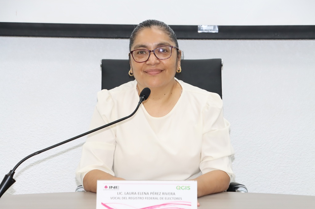 mujer de lentes y cabello recogido sentada frente a un micrófono