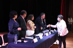 dos mujeres y dos hombres de pie frente a una mesa, uno saluda a una mujer