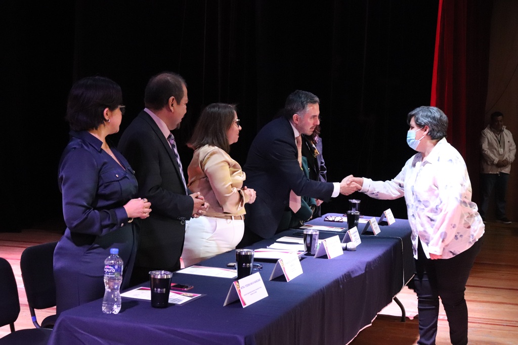 dos mujeres y dos hombres de pie frente a una mesa, uno saluda a una mujer