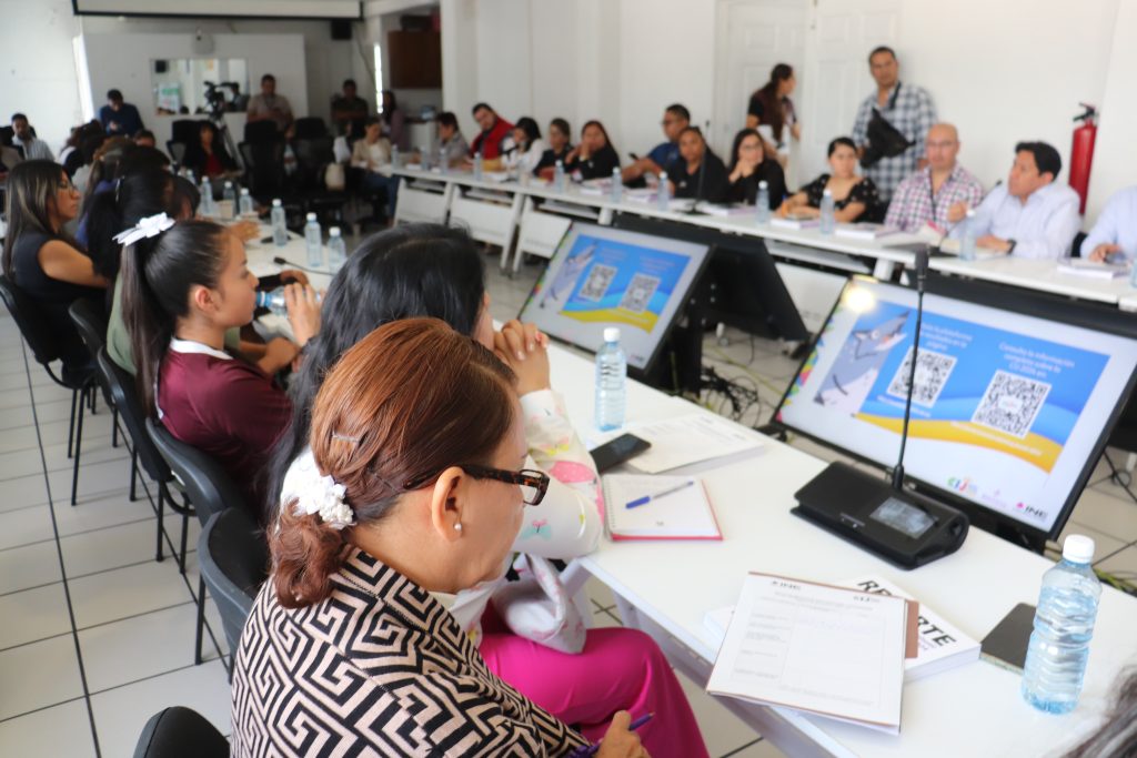 muchas personas sentadas alrededor de mesas blancas con computadoras