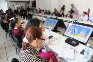 muchas personas sentadas alrededor de mesas blancas con computadoras