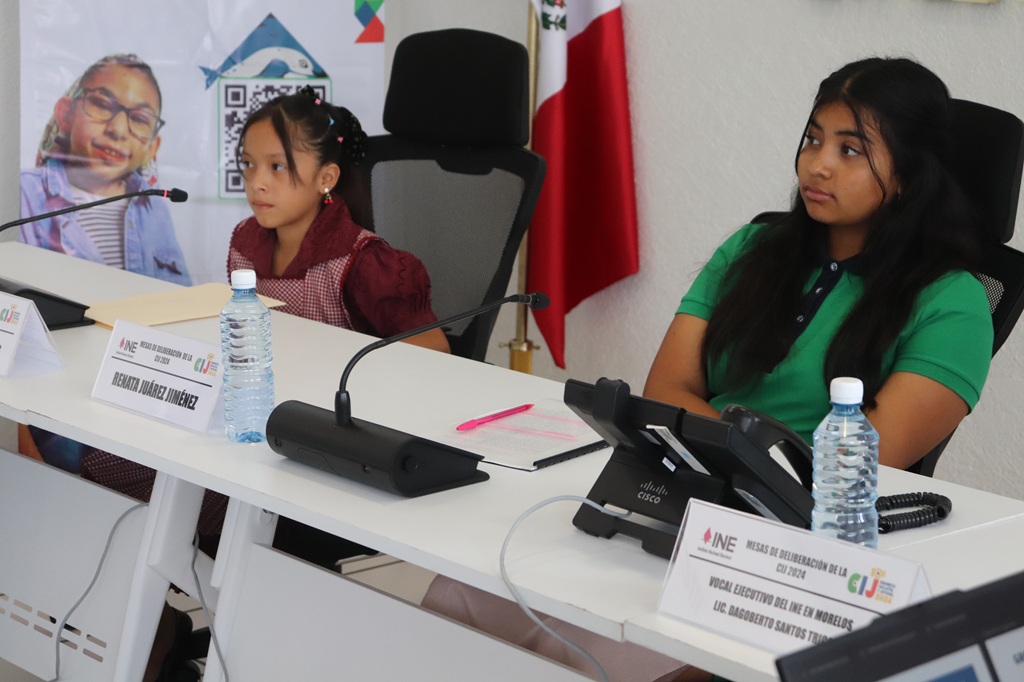 dos menores de edad sentadas en un mesa con micrófonos