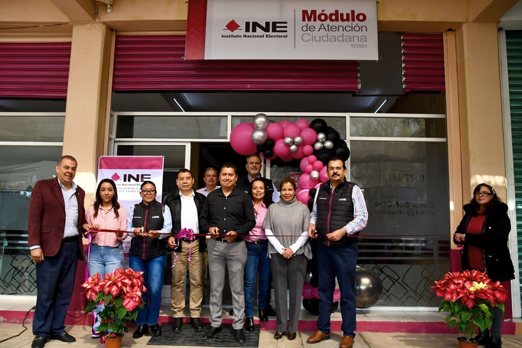 personas de pie afuera de una oficina con globos rosas y letras INE