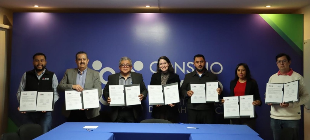 Cuatro hombres y dos mujeres de pie, sostienen un documento