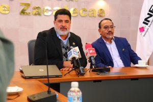 dos hombres sentados frente a una mesa con tres micrófonos