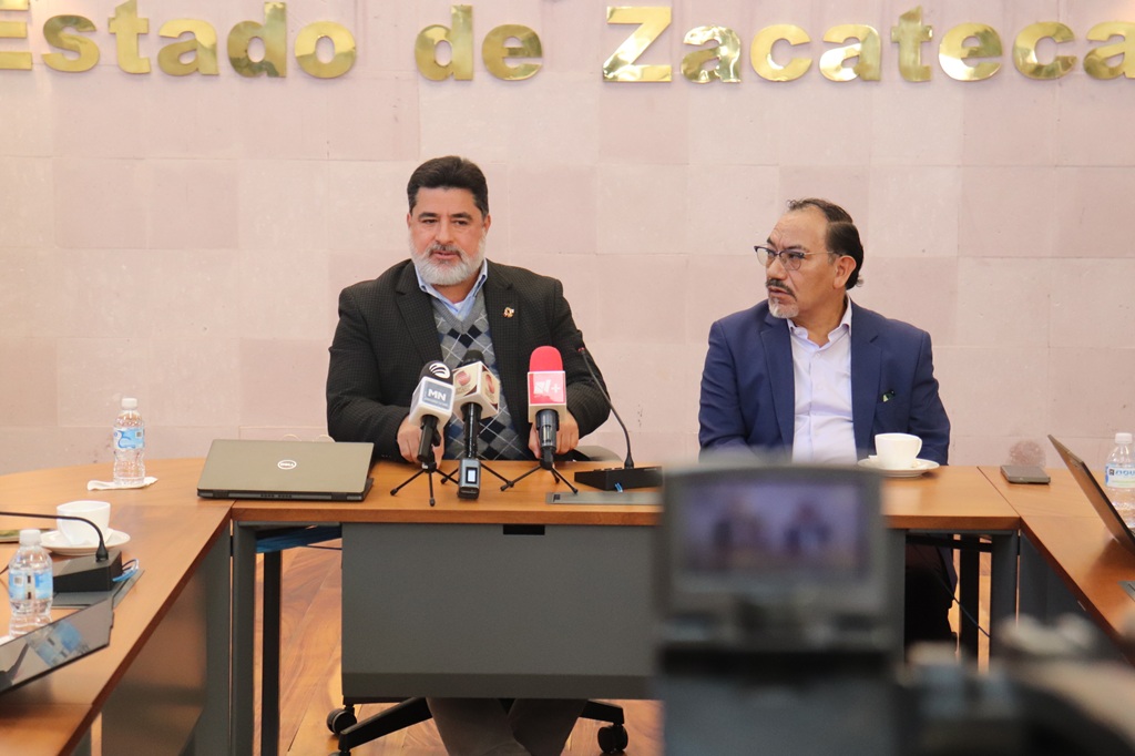 dos personas sentadas frente a una cámara de video y tres micrófonos