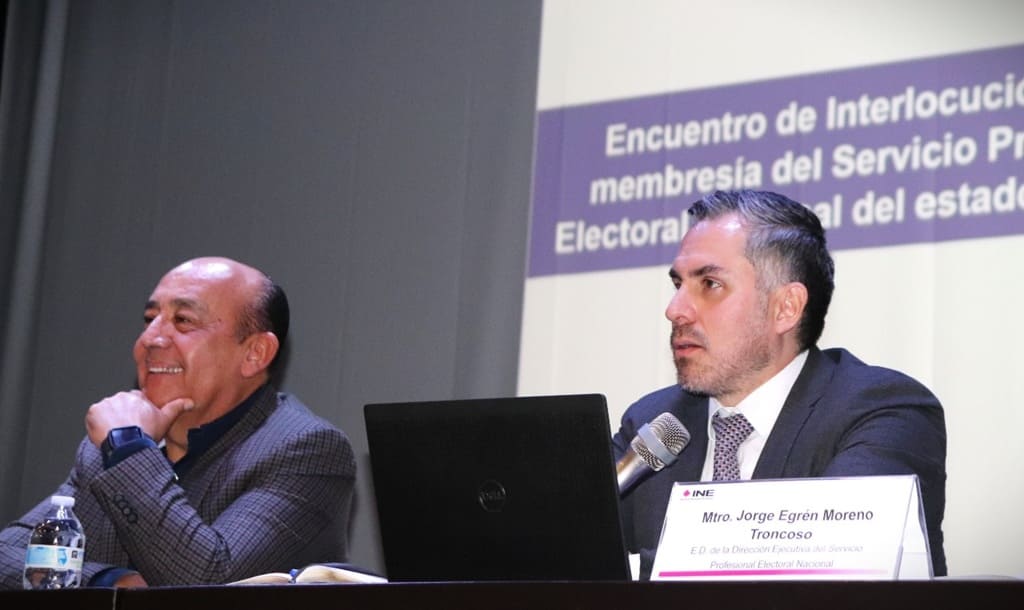 Dos hombres sentados, uno de ellos habla a través de un micrófono