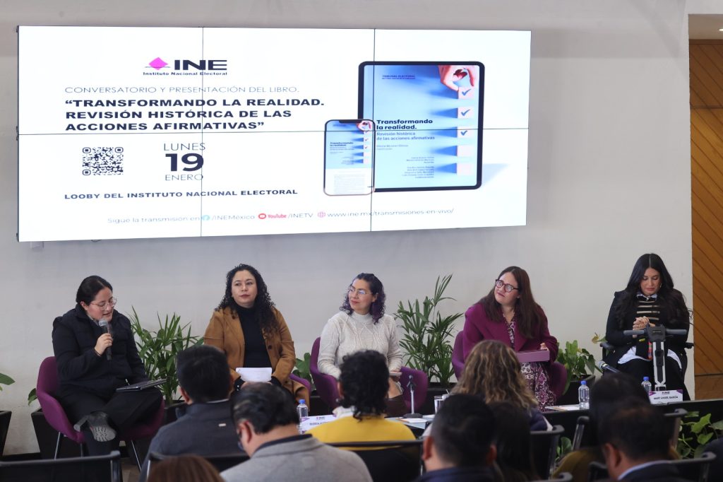 Personas participantes sentadas en el estrado del lobby del instituto frente al público asistente.