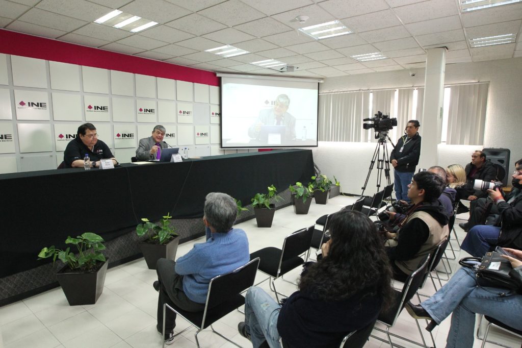 Personas participantes sentados en el estrado de la sala de prensa frente a reporteros de la fuente.
