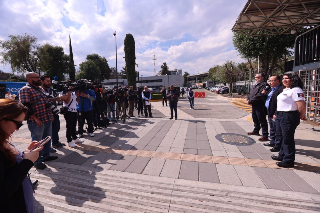 Personas funcionarias del instituto enfrente de los representantes de medios de comunicación en los torniquetes de la entrada principal.