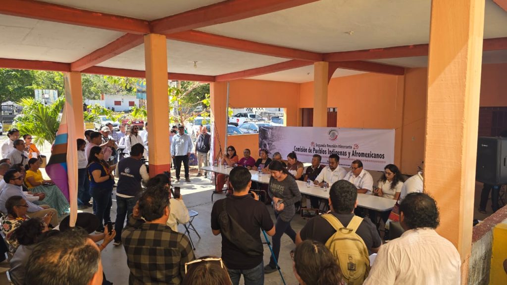 Personas participantes sentados en el estrado frente a público asistente.