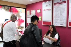 dos hombres de pie frente a una trabajadora del INE