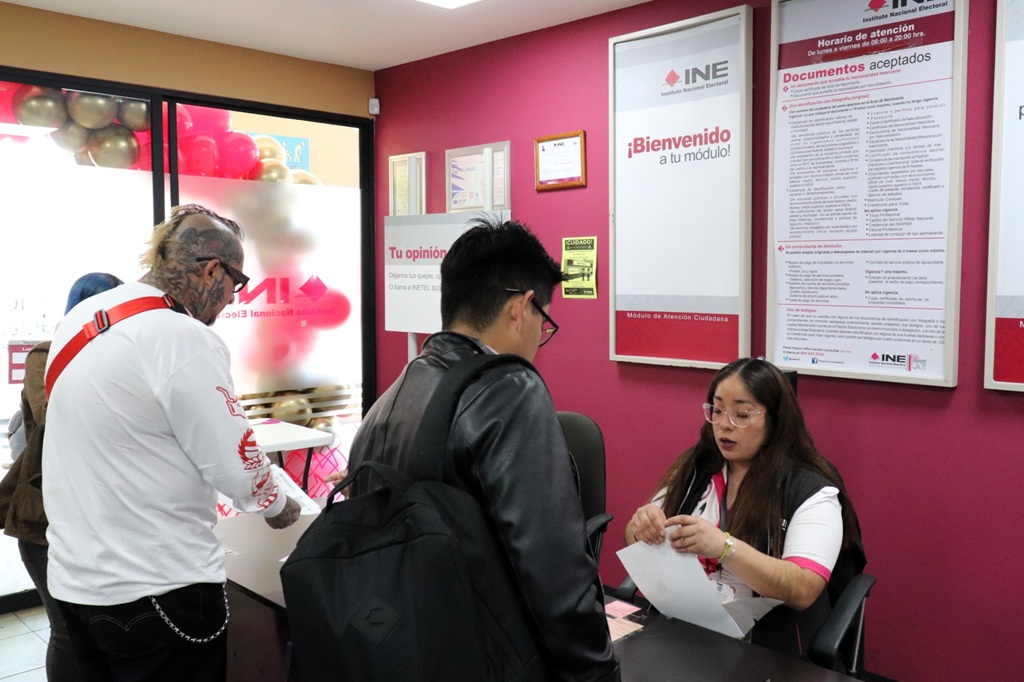 dos hombres de pie frente a una trabajadora del INE 