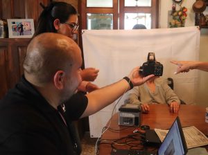 hombre sosteniendo una cámara fotográfica frente a una mujer sentada en una cama