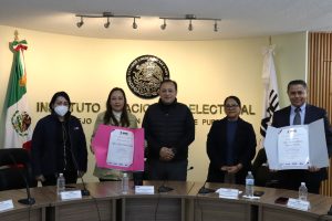 cinco personas de pie, una mujer y un hombre sostienen reconocimientos