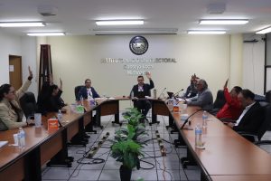 varias personas sentadas alrededor de una mesa votando a mano alzada