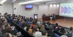 varias personas sentadas en un auditorio escuchando a una mujer que esta en el escenario