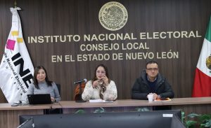 Dos mujeres y un hombre sentados frente a dos banderas