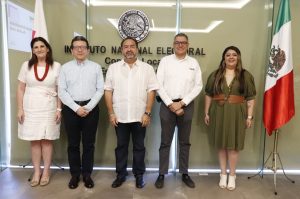 dos mujeres y tres hombres de pie a un costado de la bandera de México