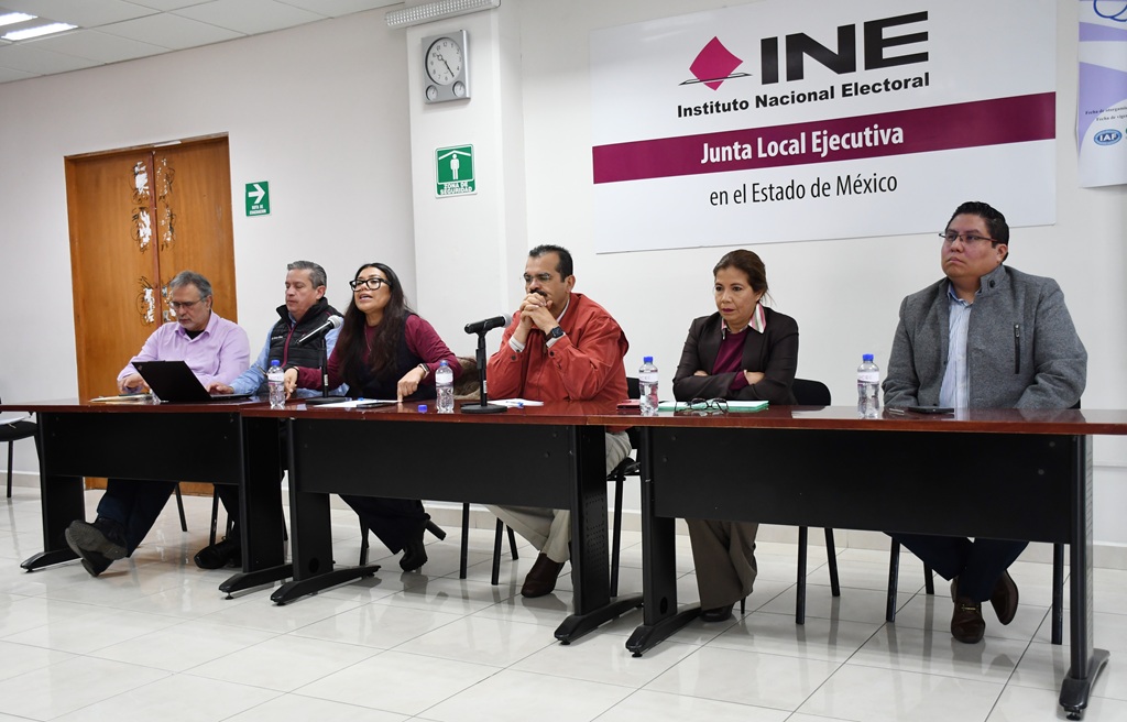 varias personas sentadas frente a un letrero que dice INE