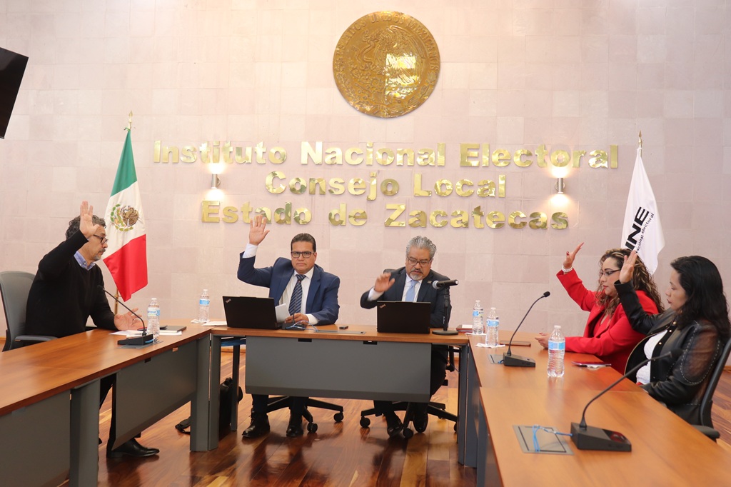 personas sentadas alrededor de una mesa rectangular votando a mano alzada