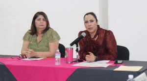 dos mujeres sentadas, una de ellas hablando frente a un micrófono