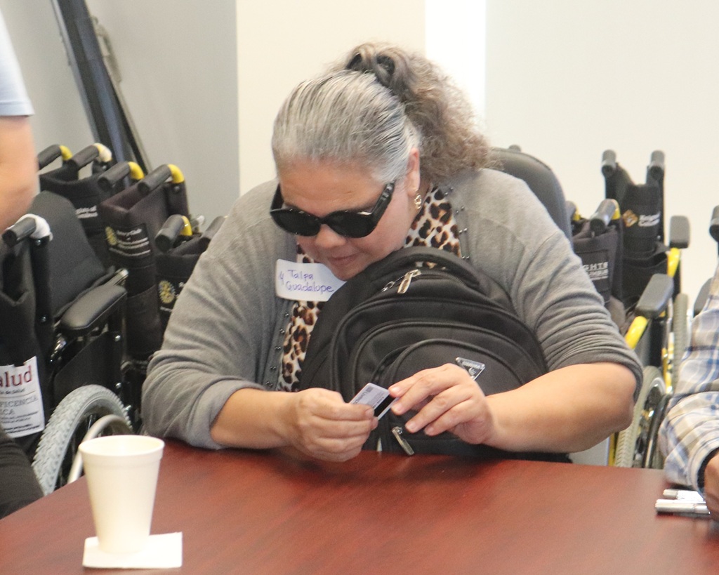 Mujer con discapacidad visual con credencial en mano y personal del INE brindando apoyo.