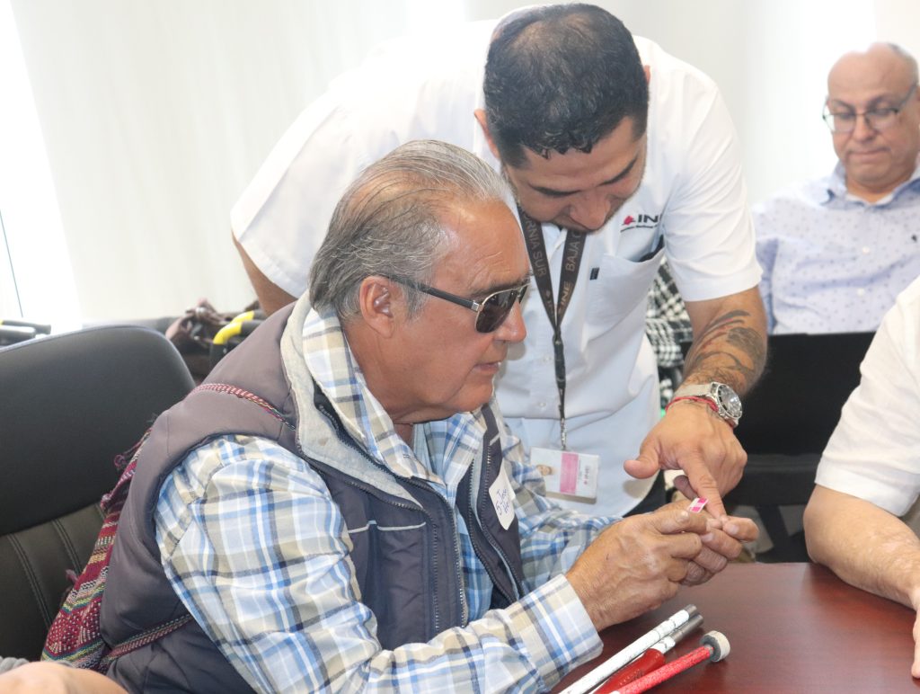 Personas con discapacidad visual con credencial en mano y personal del INE brindando apoyo.