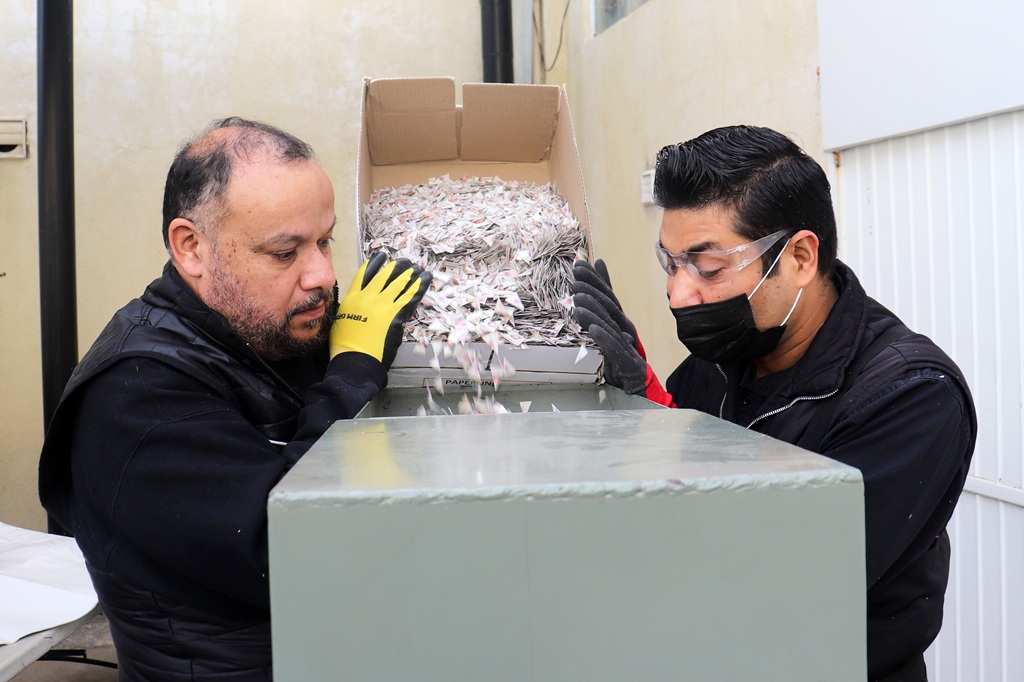 Dos hombres vaciando una caja con credenciales para votar sin validez en maquina trituradora