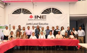 varias personas de pie y sentadas, atrás una lona con letras negras