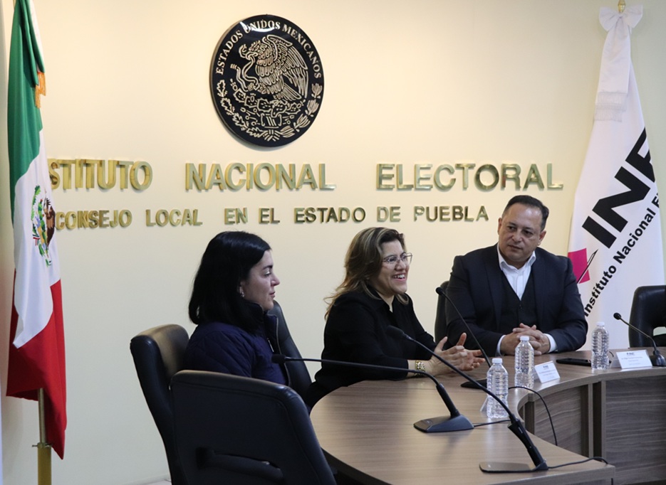 dos mujeres y un hombre sentados atrás de una mesa ovalada