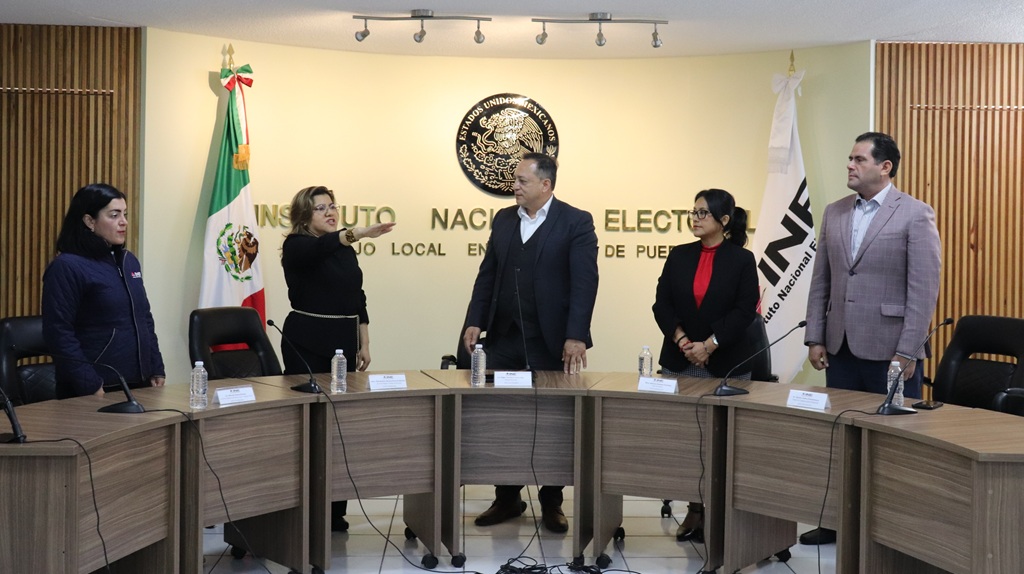 cuatro mujeres y dos hombres de pie, una de ellas con el brazo extendido hacia enfrente,