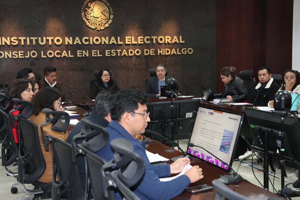 Varias personas sentadas alrededor de una mesa con micrófonos y computadoras