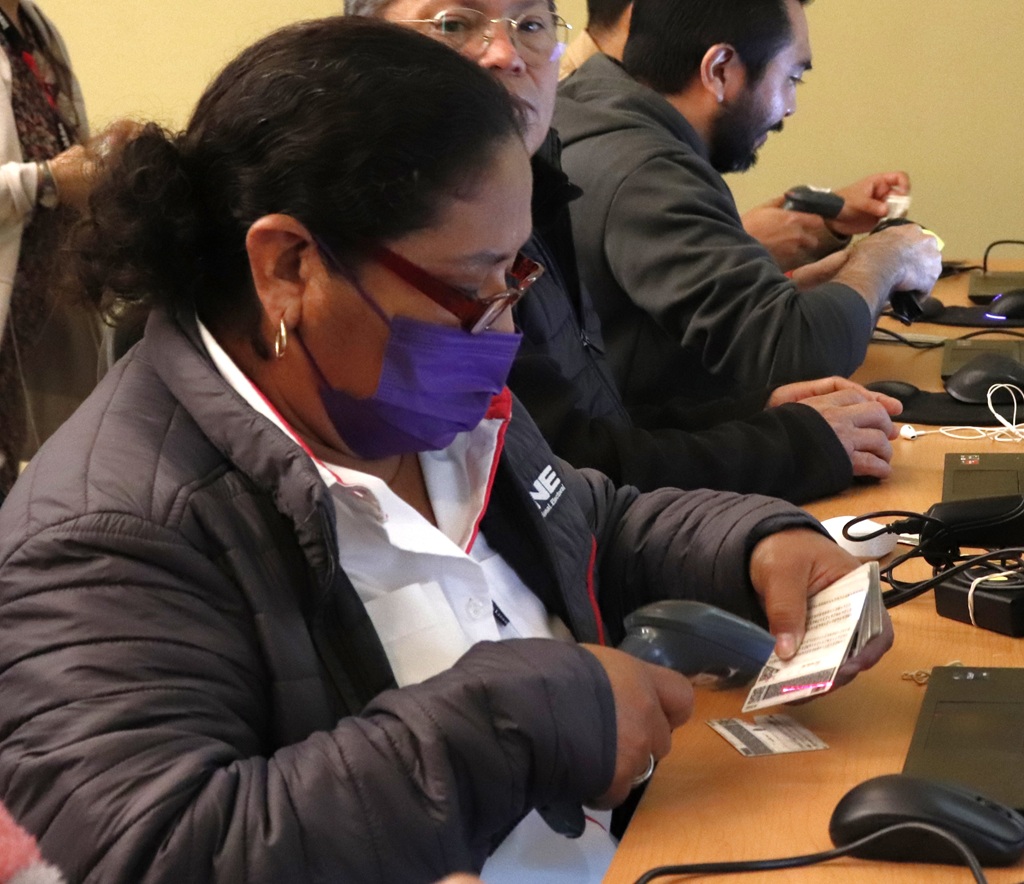 mujer con cubrebocas colocando un lector de código de barras sobre una credencial para votar