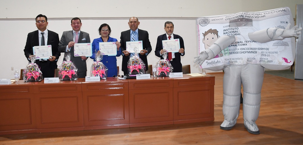 cuatro hombres y una mujer sosteniendo un documento a lado una botarga de credencial