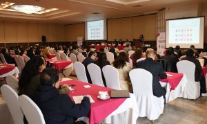 muchas personas sentadas en un salón mirando una pantalla