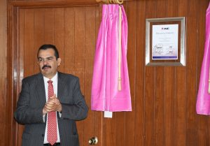 Un hombre de lentes, traje y bigote de pie a un lado de un reconocimiento