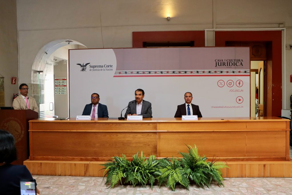 tres hombres sentados frente a una mesa en un pódium