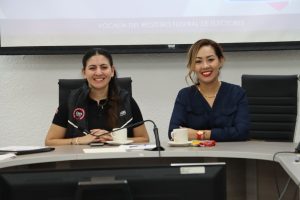 dos mujeres sentadas con camisa negra y cabello recogido