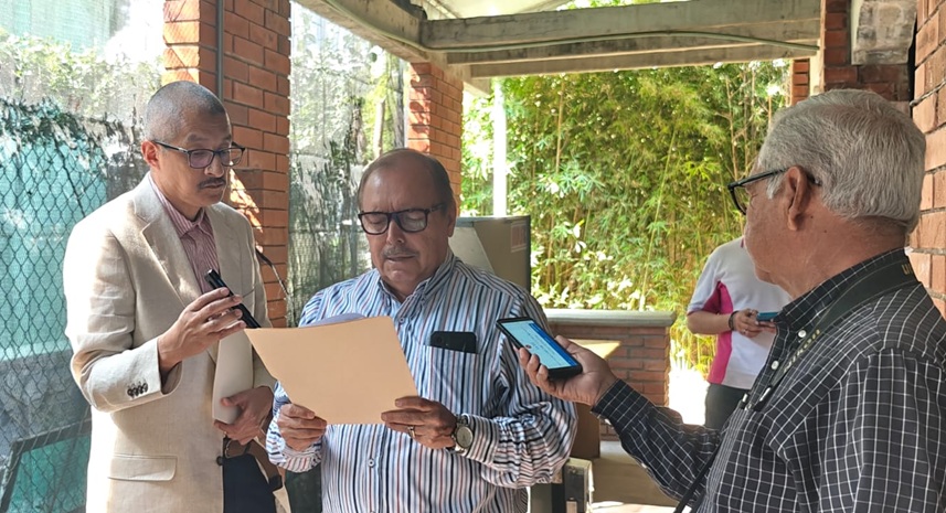tres hombres uno leyendo y dos sosteniendo celulares frente al que habla