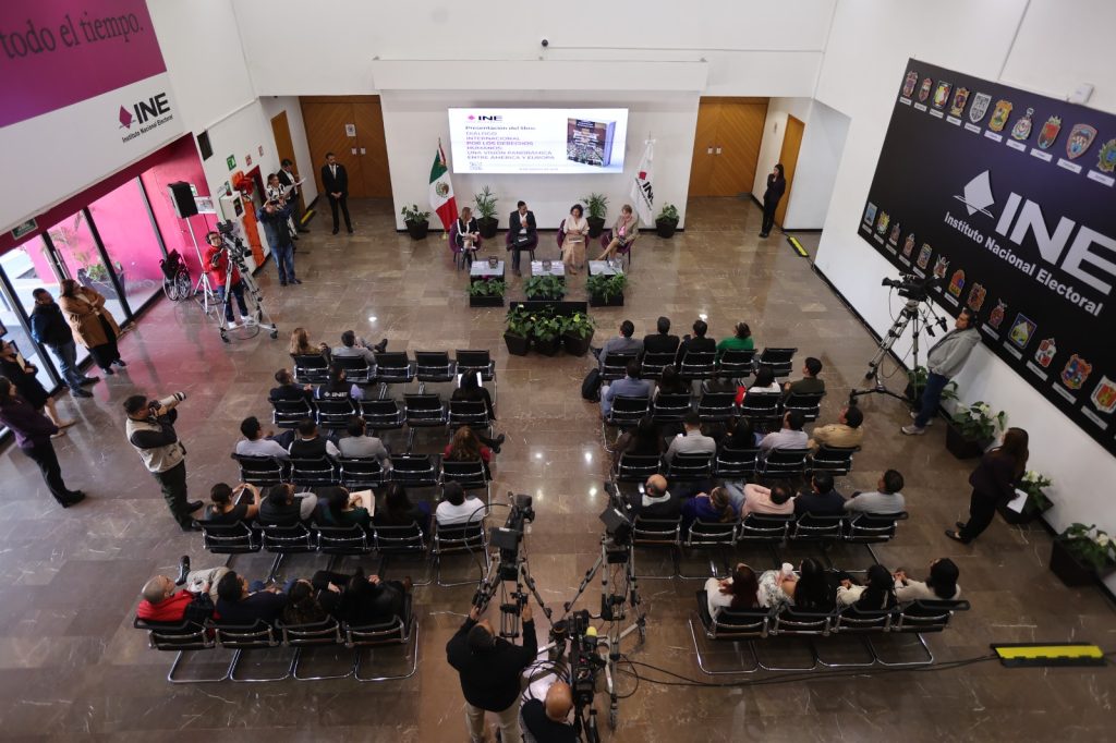 Toma abierta aérea del Lobby con las personas participantes enfrente del público asistente.