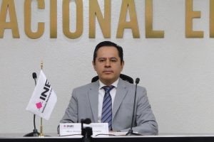 Hombre vestido de traje gris, sentado detrás de un micrófono