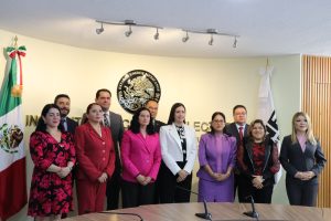 varias personas de pie frente al escudo nacional de México